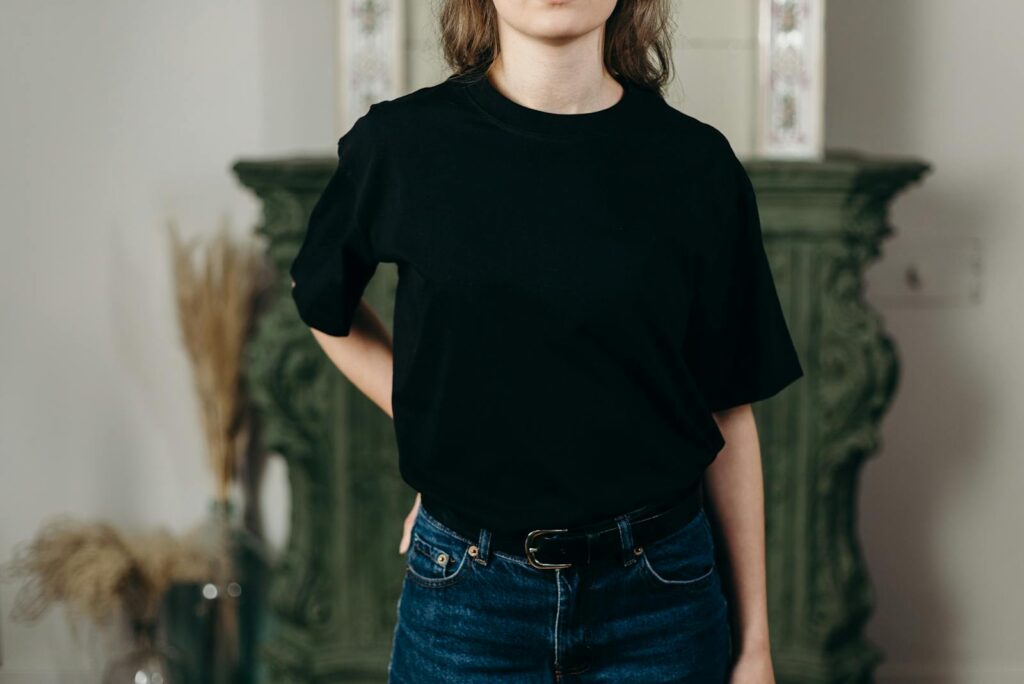 Faceless model in black t-shirt and jeans showcasing minimalist fashion style indoors.