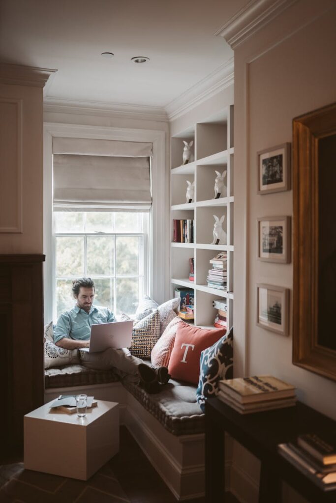 A person working remotely on a laptop in a cozy home office nook with bookshelves.