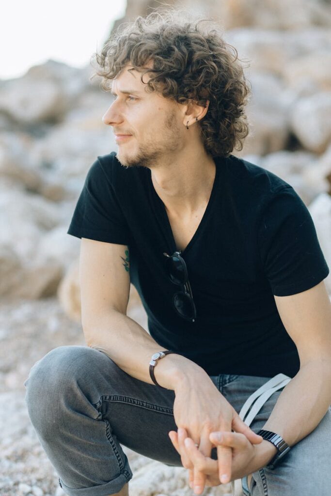 Casual man in black shirt and jeans sitting on rocks, enjoying nature.