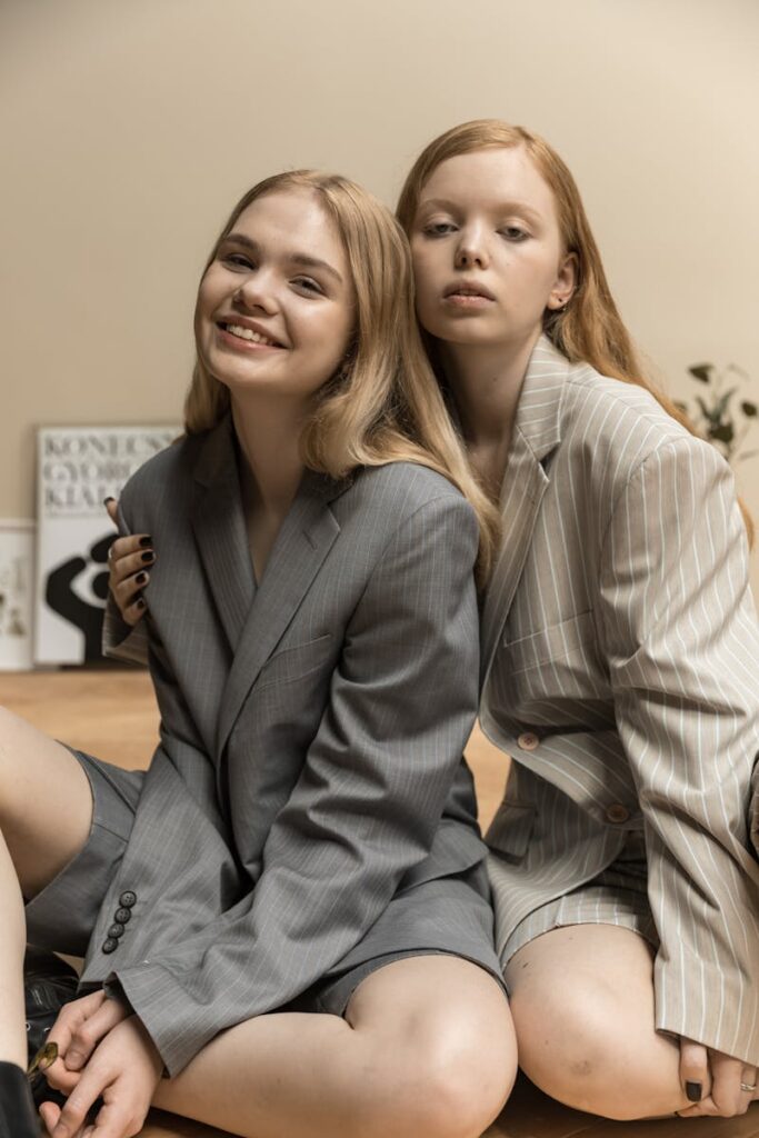 Two women in suits sharing a casual, friendly moment indoors.