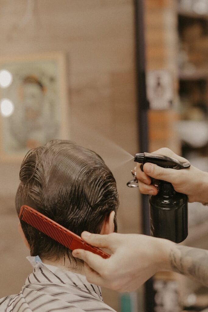 Hairdresser using a comb and spray bottle to style hair in a barbershop setting.