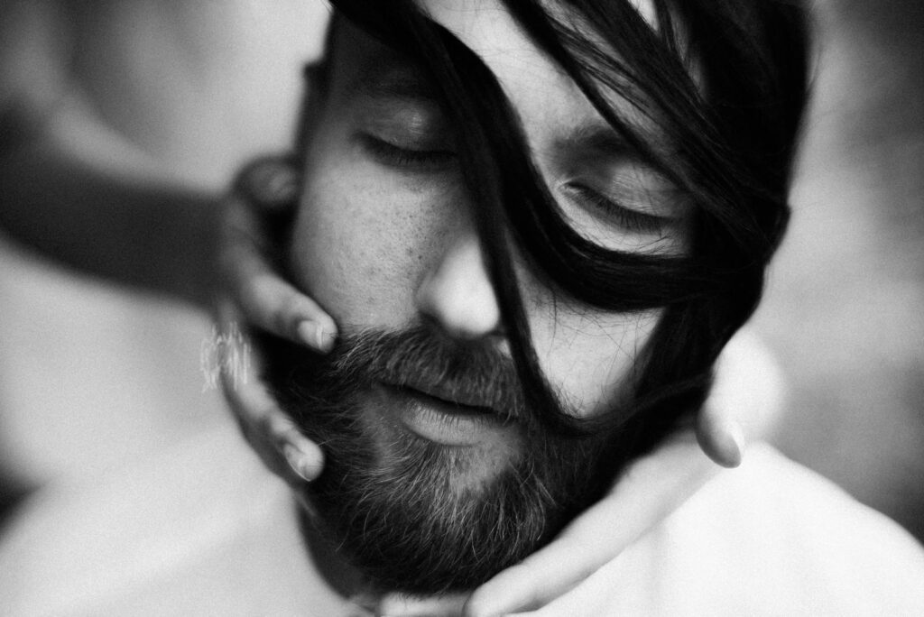 Close-up monochrome portrait of a serene bearded man with eyes closed, hair in the wind.