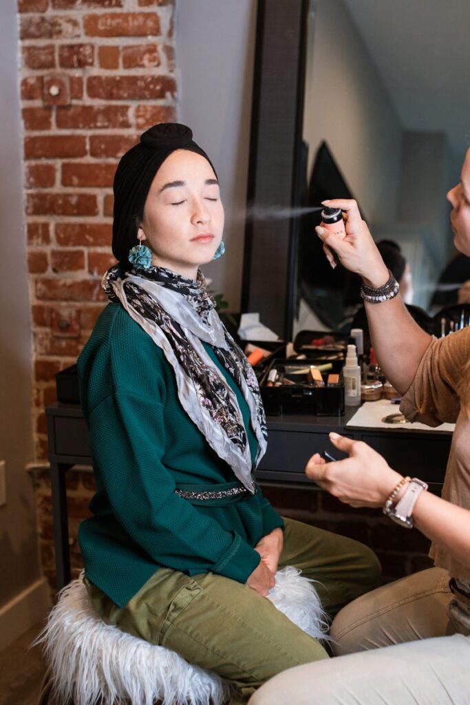 Makeup artist applying spray on a hijabi woman in a studio setup.