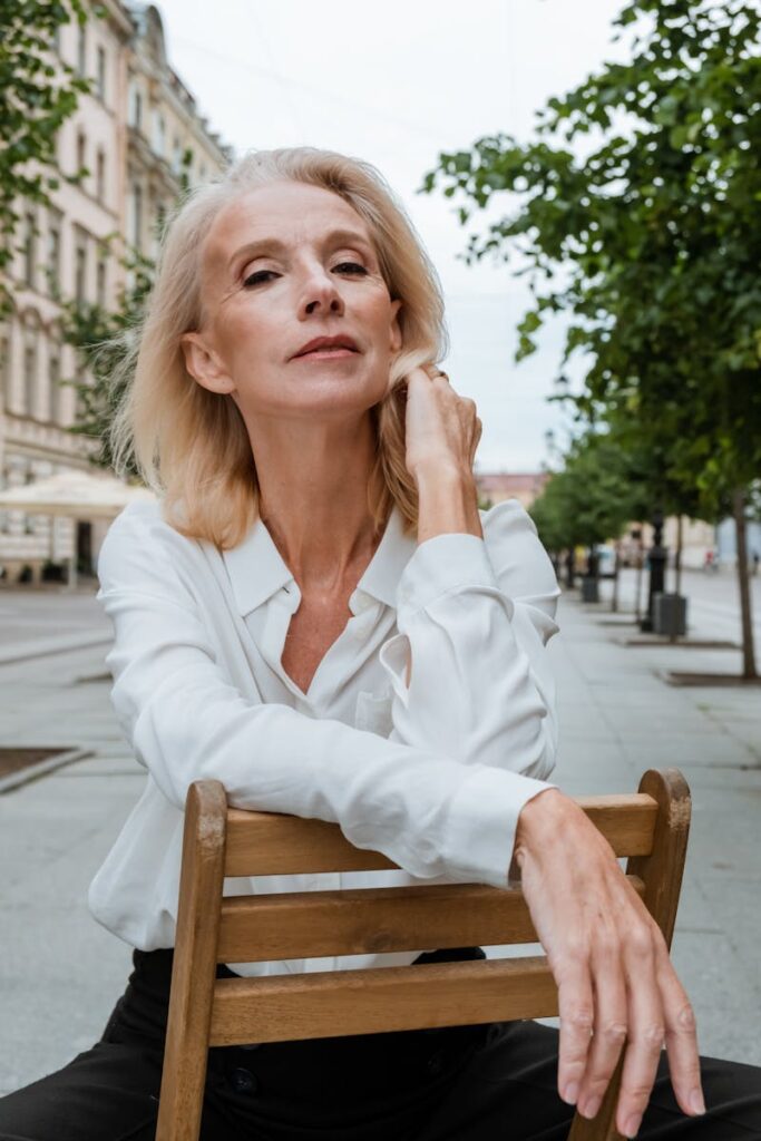 Stylish elderly woman in white shirt posing outdoors in cityscape.