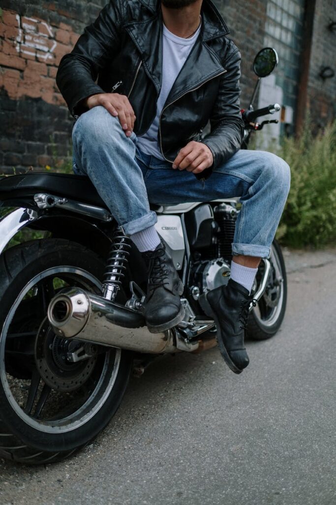 Stylish man sitting on a motorcycle wearing jeans and a leather jacket.