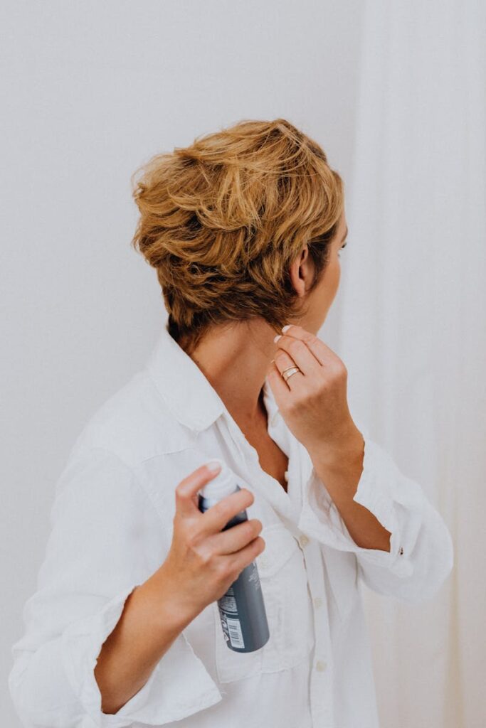 Back view of a woman styling short hair with hairspray, showcasing casual elegance.