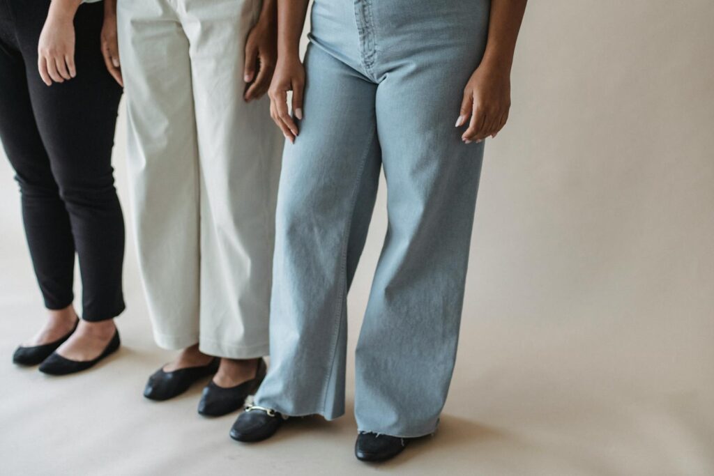 Three women standing in stylish pants showcasing diverse fashion on a neutral background.