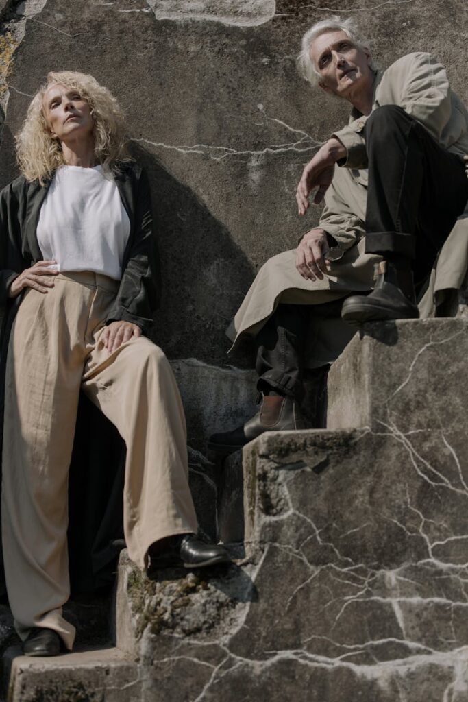 Fashionable senior couple in trench coats striking a pose on ancient stone steps outdoors.
