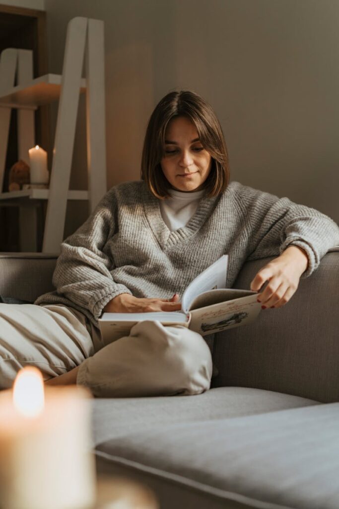 Woman in a cozy sweater reading a book on a comfortable sofa, creating a warm, serene atmosphere.