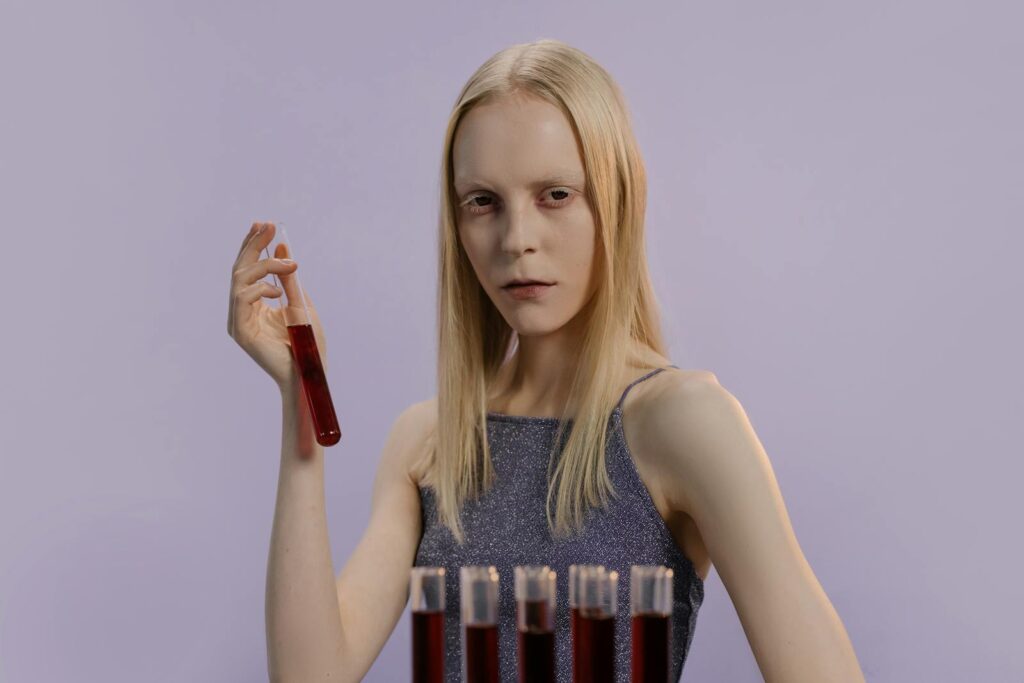 Blonde woman holding a vial with red liquid, set against a purple background.