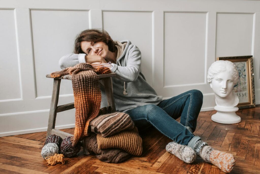 Woman relaxing indoors with knitting materials and wearing cozy clothes.