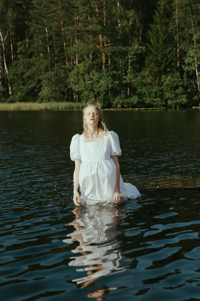 A serene scene of a woman in a white dress standing in a lake, surrounded by forest.