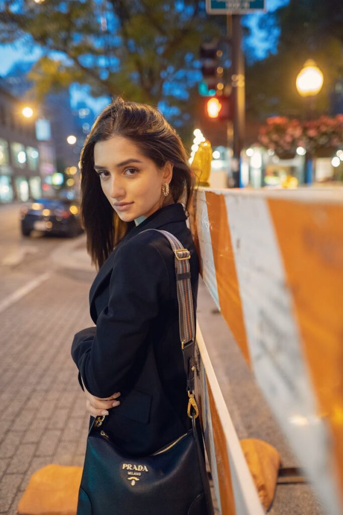 Elegant woman in a blazer leaning against a barricade on an evening city street.