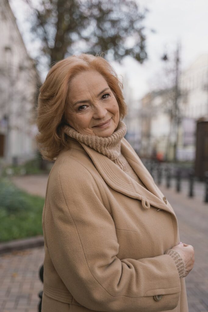 Smiling senior woman in beige coat and turtleneck enjoying a stroll outdoors in fall.