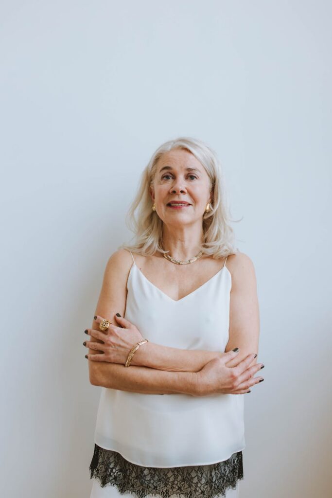 Sophisticated senior woman with gray hair smiling confidently against a plain background.