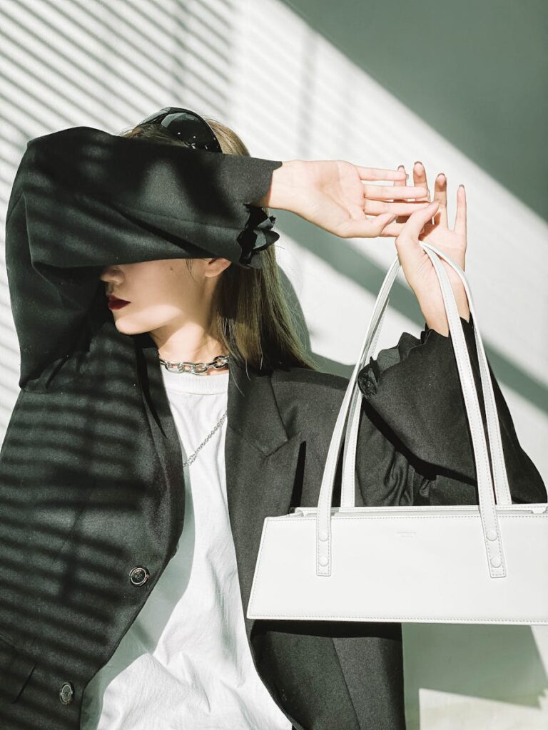 Elegant woman in black blazer holding a white handbag, embodying modern fashion trends.