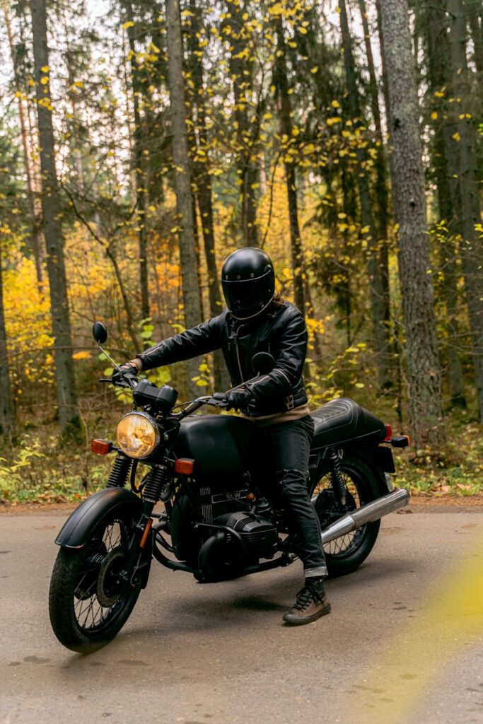 A motorcyclist wearing a helmet and leather jacket rides through a serene autumn forest.