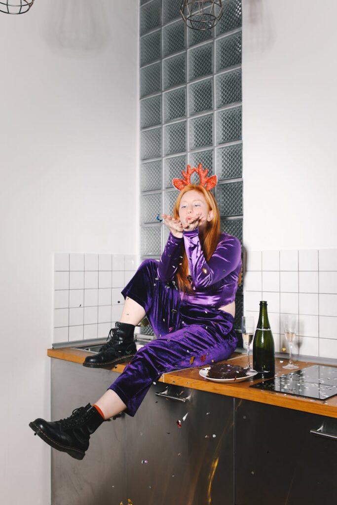 Red-haired woman in purple sitting on kitchen counter celebrating New Year indoors.