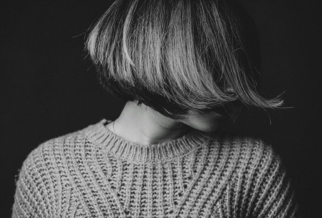 Striking black and white portrait of a woman with obscured face, wearing a textured sweater.