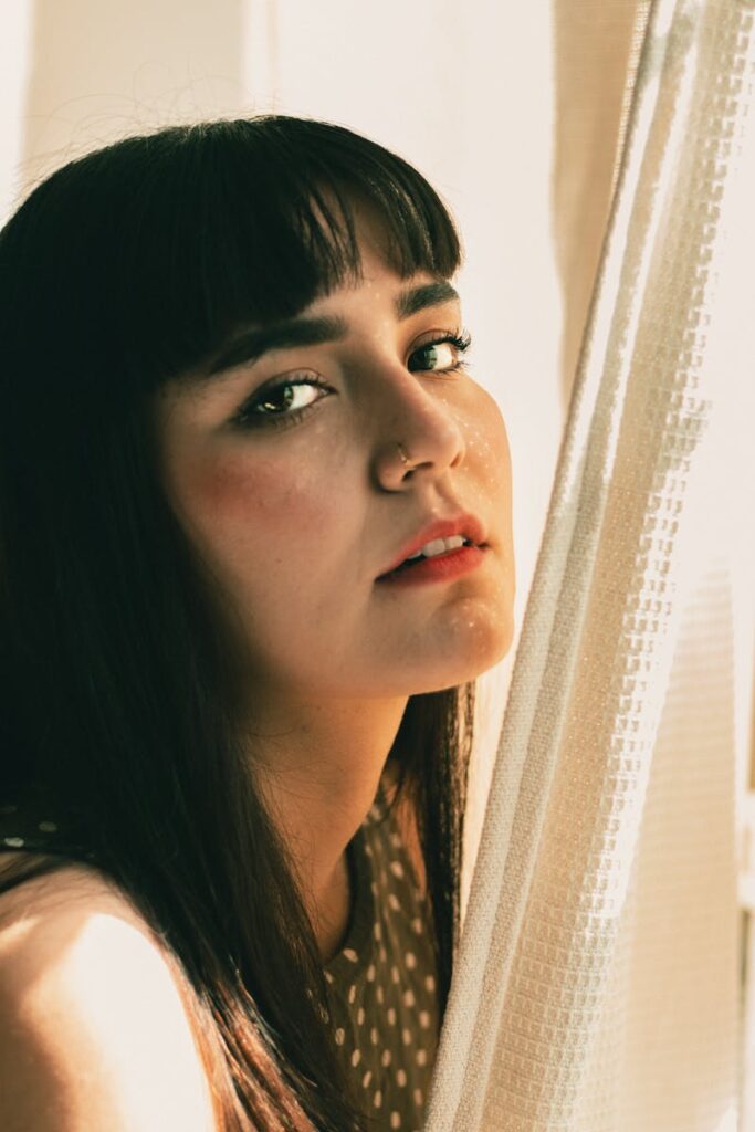 Close-up portrait of a woman with bangs lit by natural sunlight indoors.