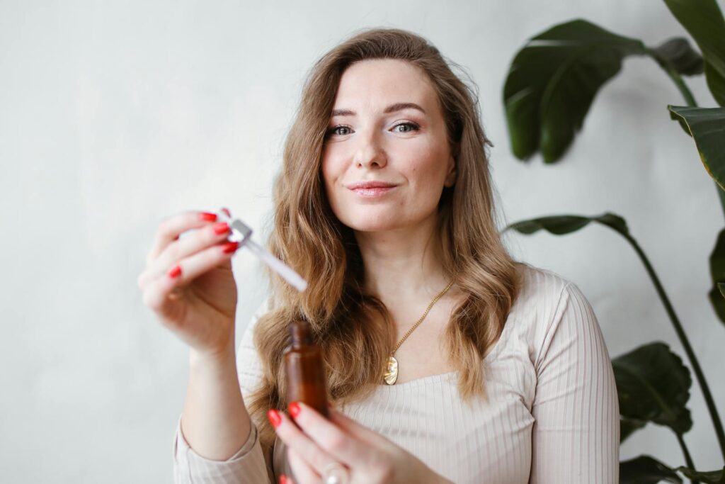 Woman applying skincare serum with dropper near indoor plants.