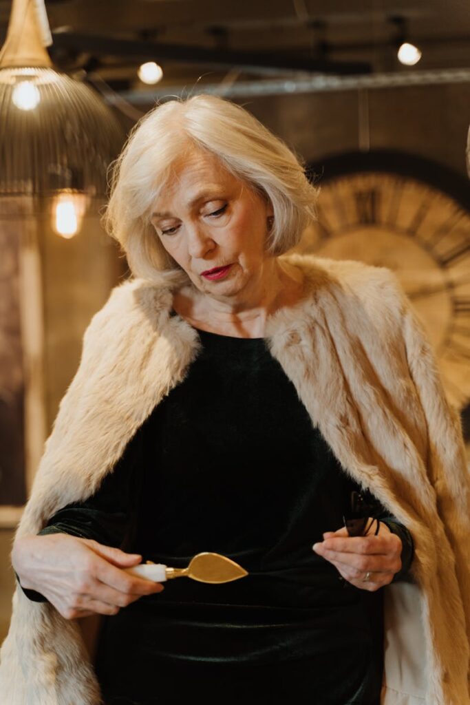 Sophisticated senior woman in a luxurious fur coat and black dress examining a chisel indoors.