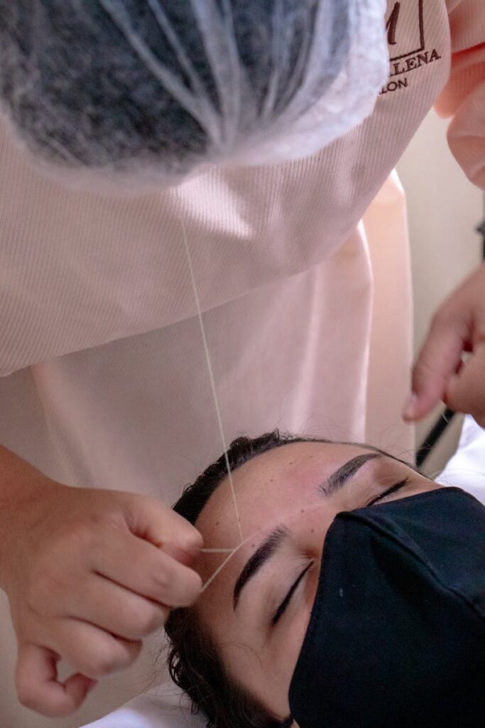 Close-up of eyebrow threading procedure in a salon, highlighting beauty and precision.