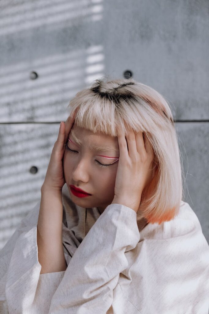 Portrait of a woman with closed eyes and hands on head, feeling stressed.