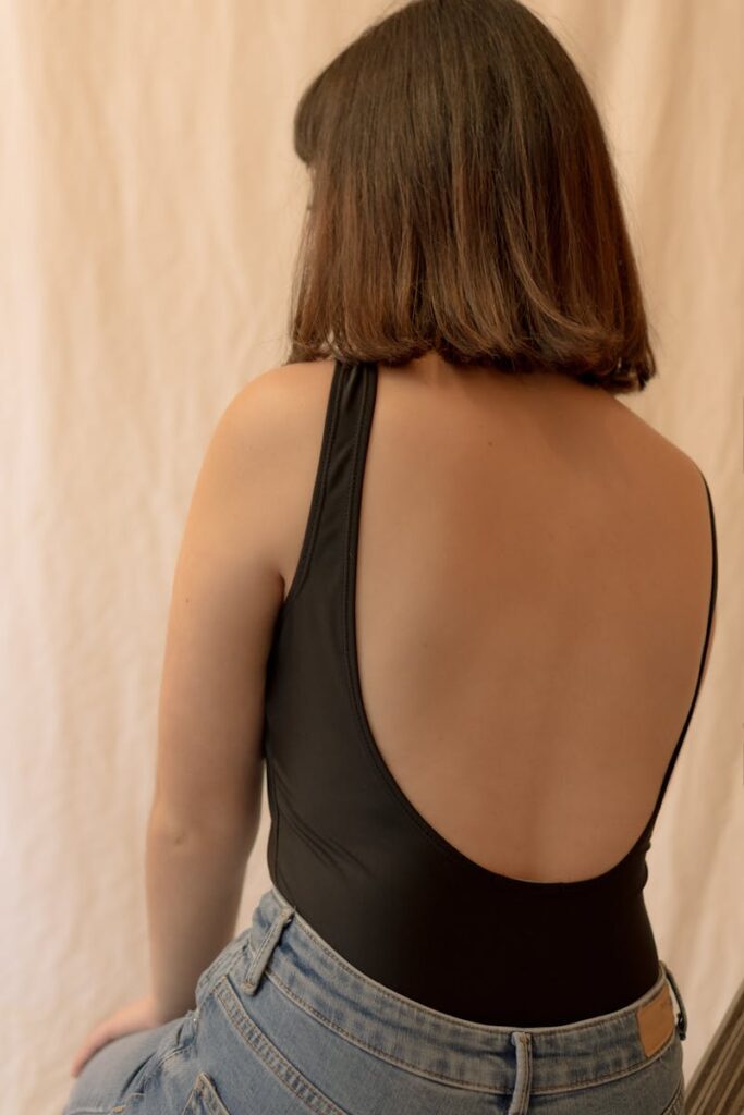 A back view portrait of a woman wearing a stylish black top, taken indoors.