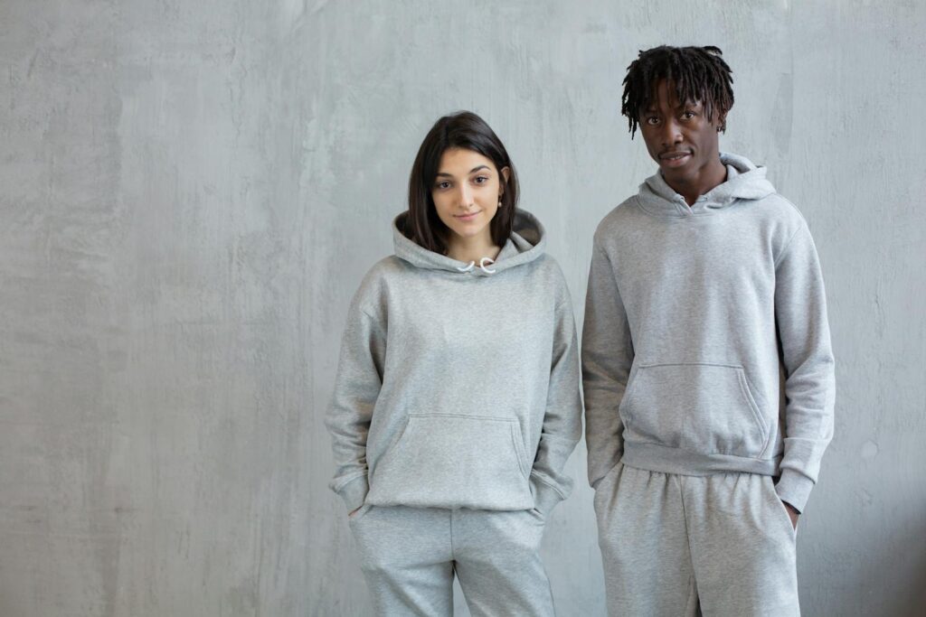 Smiling diverse man and woman wearing similar sports suits standing with hands in pockets and looking at camera