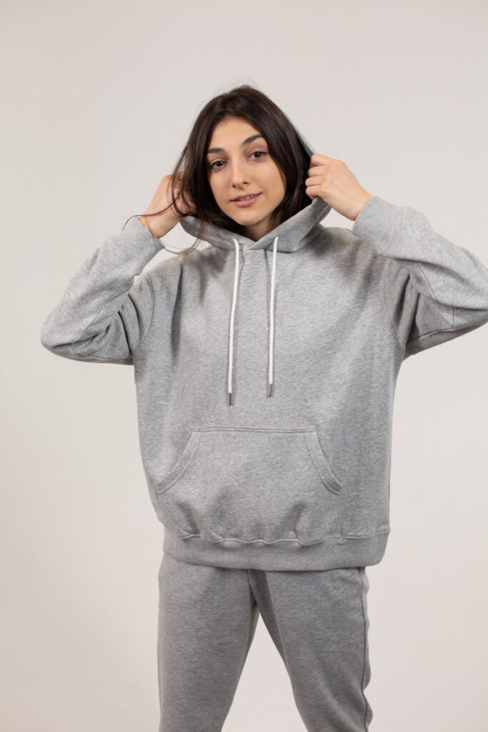 A contemporary studio portrait of a confident young woman wearing a gray hoodie and sweatpants.