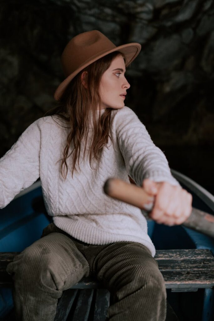 Young woman wearing a hat rowing a boat through a dimly lit cave, capturing an essence of adventure and exploration.