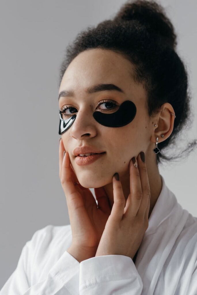 Portrait of a woman with curly hair applying under eye masks, emphasizing self-care and skincare routine.