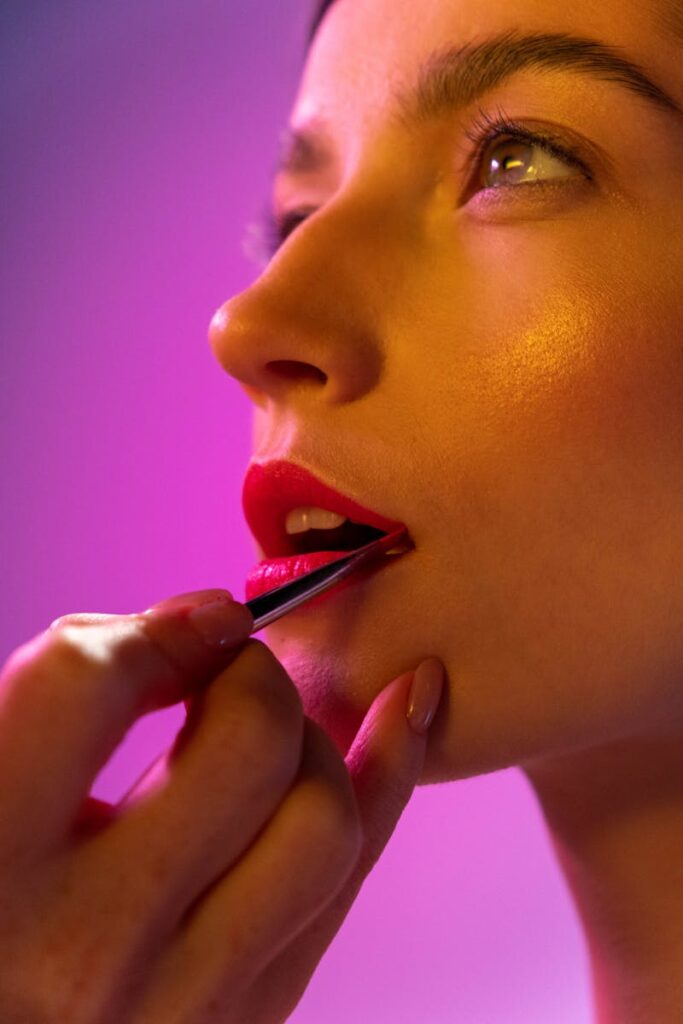 Close-up of a woman receiving professional lipstick application with vibrant lighting.