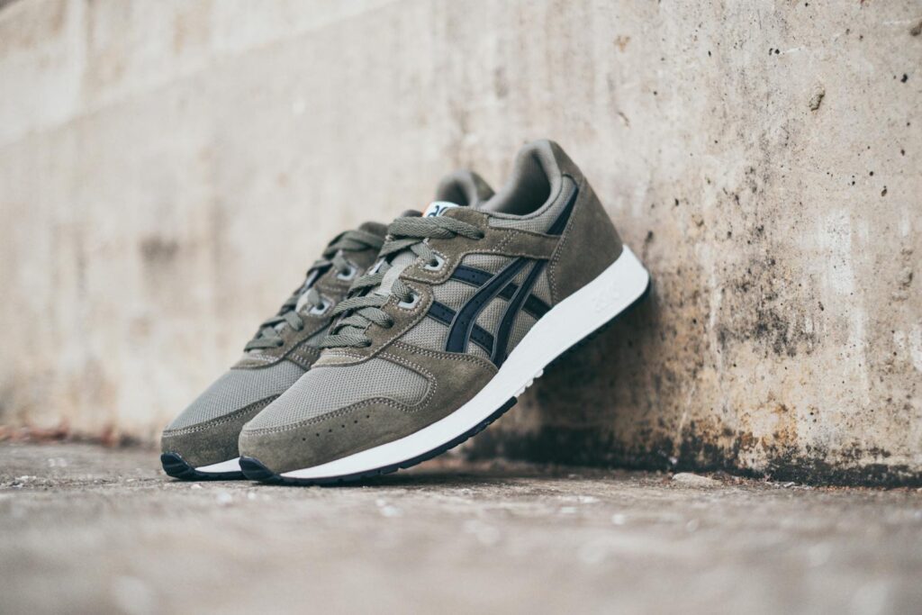 Pair of green sneakers with black details leaning against a concrete wall.