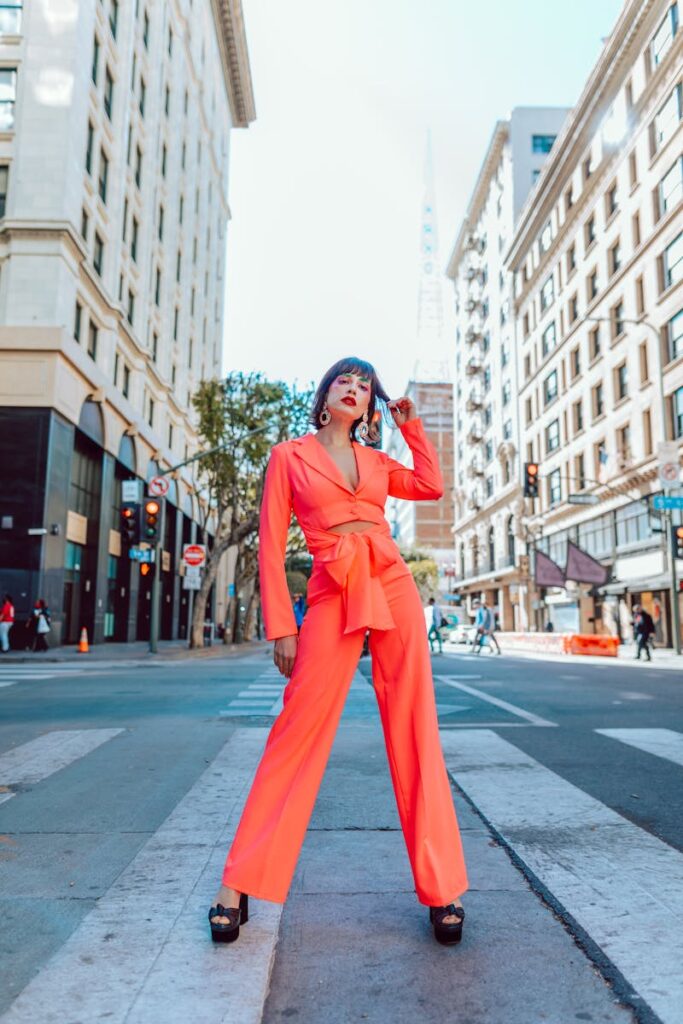 A fashionable woman in bright orange attire posing confidently on a city crosswalk.
