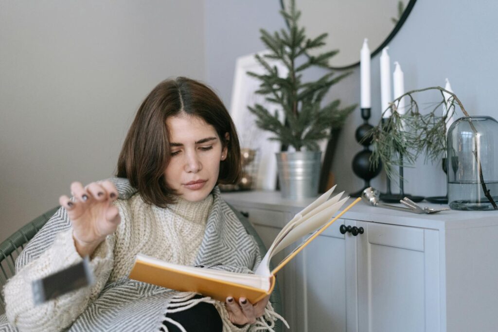 A woman in a knitted sweater enjoys reading a book at home, surrounded by cozy decor.