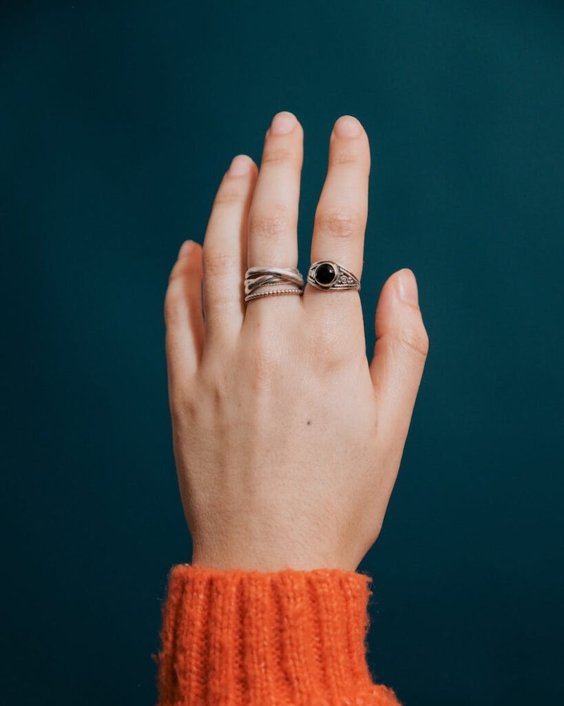 Overhead view of crop faceless female in orange sweater showing vintage rings on fingers on blue background
