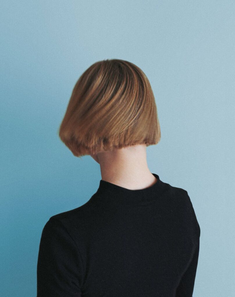 Minimalist portrait of a person with short hair, seen from the back against a blue background.