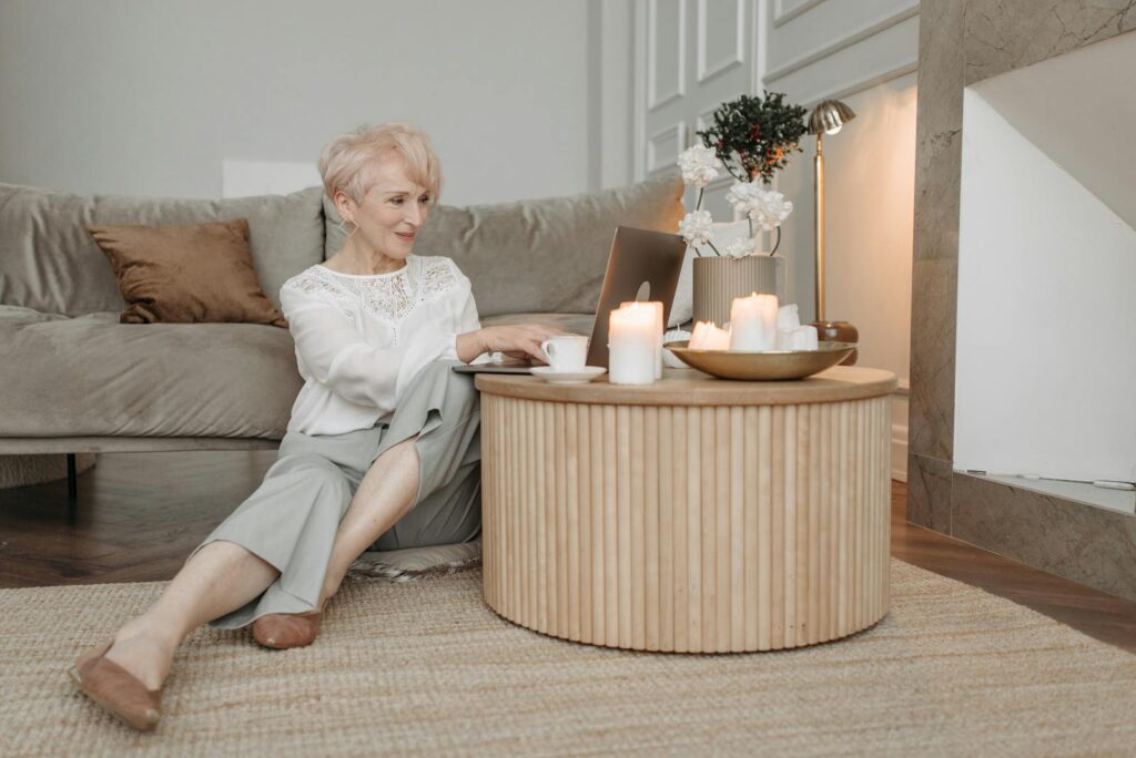 Elegant senior woman working on a laptop in a stylish living room setting, surrounded by candles.