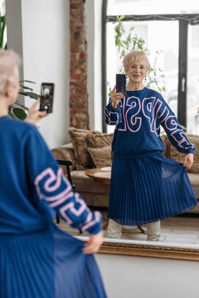 Senior woman takes a playful mirror selfie indoors, showcasing laughter and style.