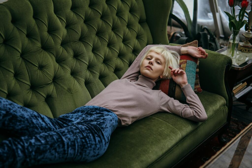 Blonde woman with short hair relaxing on a vintage green sofa indoors.