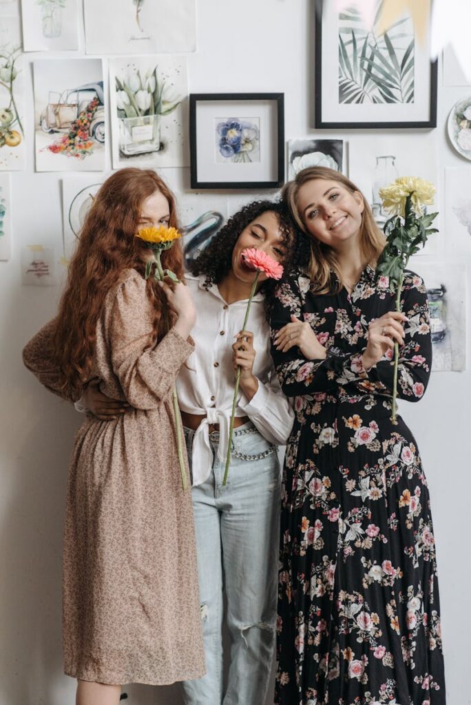 Three women smiling with flowers in a cozy artistic workspace showcasing friendship and creativity.