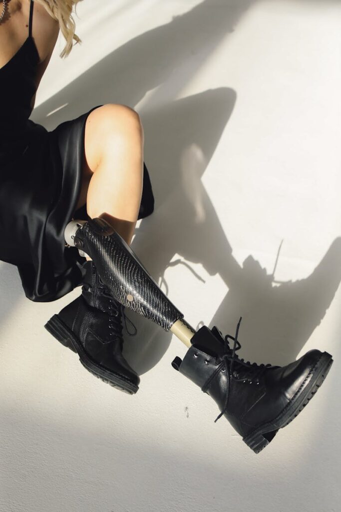 Model with a prosthetic leg in leather boots and black dress showcasing fashion and empowerment.