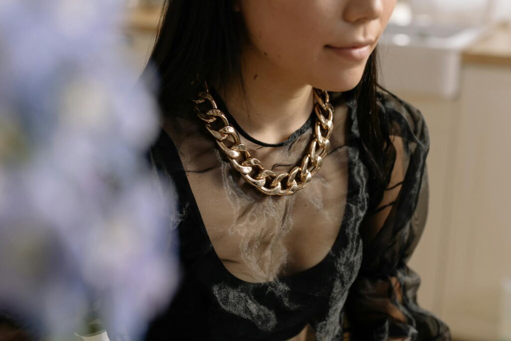 Portrait of a woman wearing a chunky gold necklace and sheer top indoors.