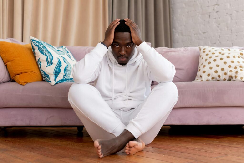 Adult male in casual white outfit sitting pensively in a cozy living room.