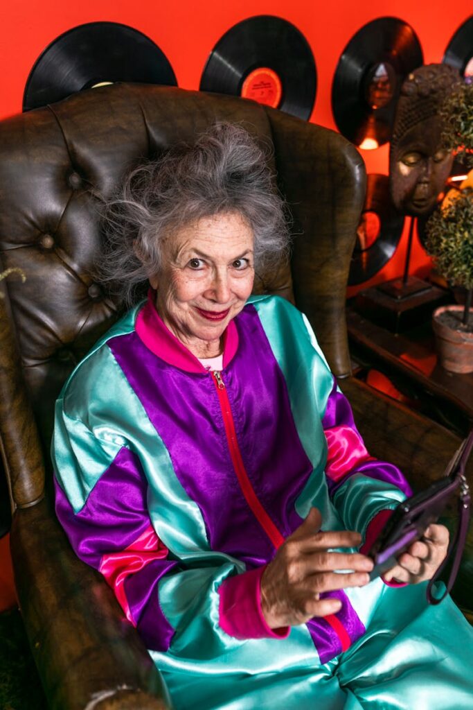 Playful senior woman in a vibrant tracksuit using a smartphone indoors.