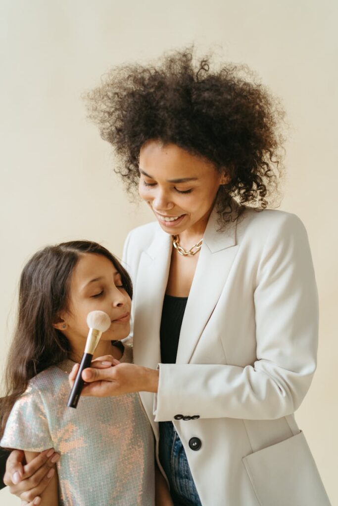 Smiling mother applying makeup to daughter, showcasing family bonding and happiness.