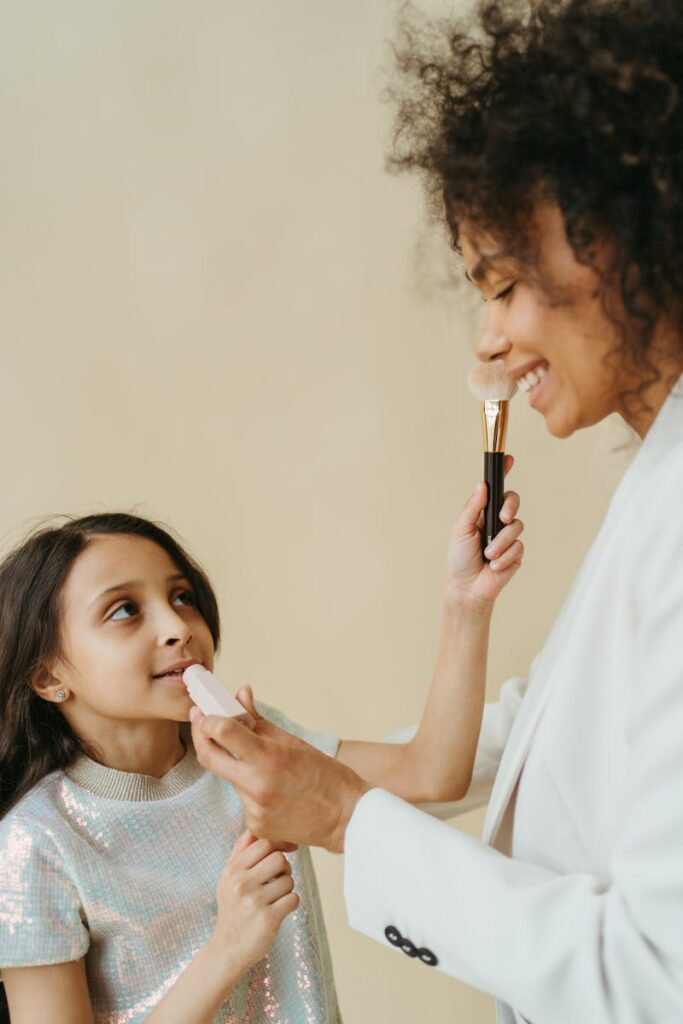A joyful mother and daughter bonding over makeup in a warm, indoor setting.