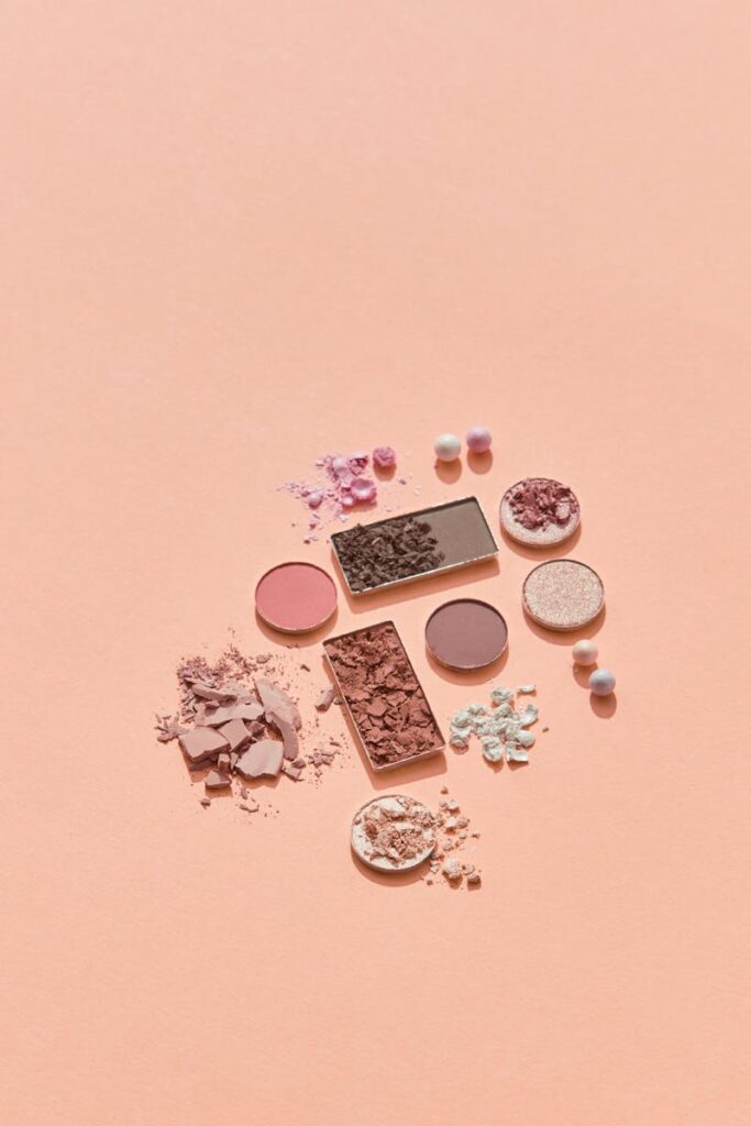 Artistic flat lay of crushed and pressed eyeshadows on a soft peach background, perfect for beauty blogs.